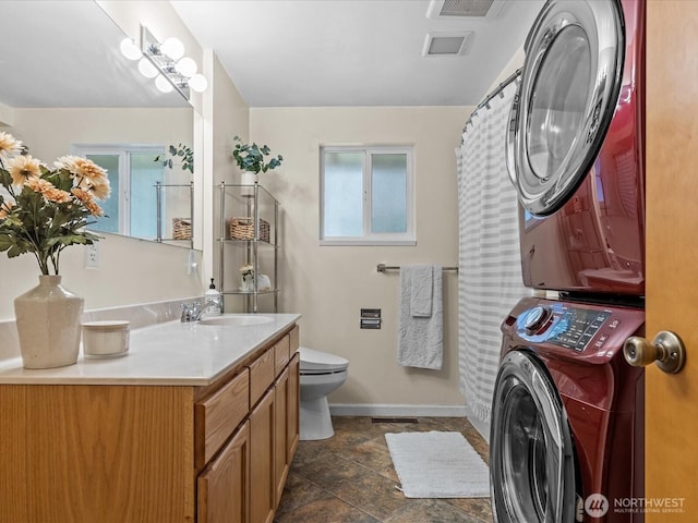 full bathroom with vanity, stacked washer and dryer, toilet, and baseboards