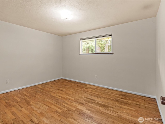 spare room featuring a textured ceiling, light wood-type flooring, and baseboards