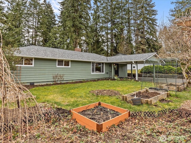 rear view of property featuring a lawn, a vegetable garden, a chimney, and roof with shingles