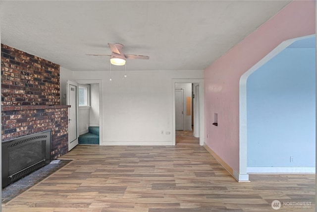 unfurnished living room featuring heating unit, wood finished floors, a fireplace, baseboards, and ceiling fan