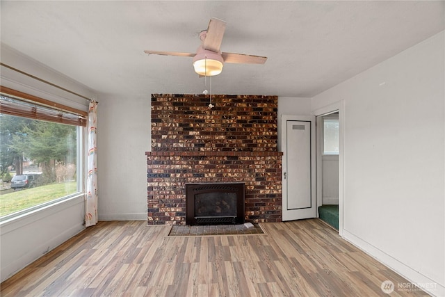 unfurnished living room with a fireplace, a ceiling fan, baseboards, and wood finished floors