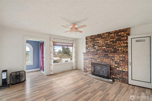 unfurnished living room featuring a brick fireplace, wood finished floors, and baseboards