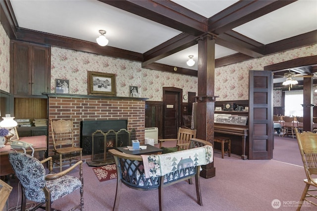 carpeted living area featuring beamed ceiling, wallpapered walls, ceiling fan, wainscoting, and a brick fireplace