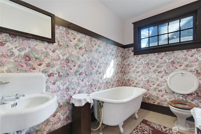 bathroom featuring wallpapered walls, toilet, a sink, and a freestanding bath