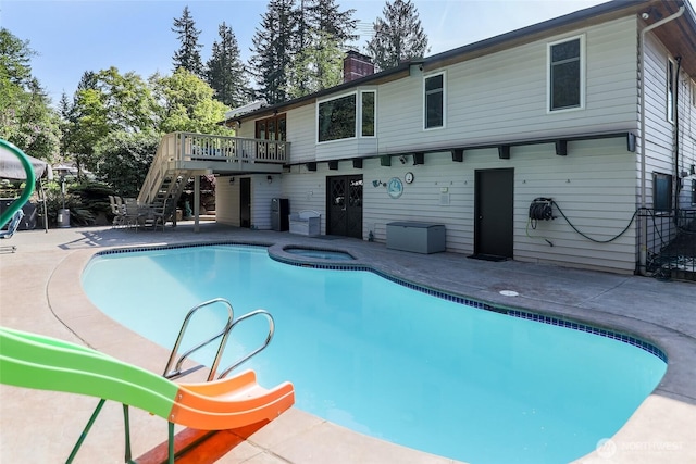 pool with stairway, a wooden deck, an in ground hot tub, and a patio area