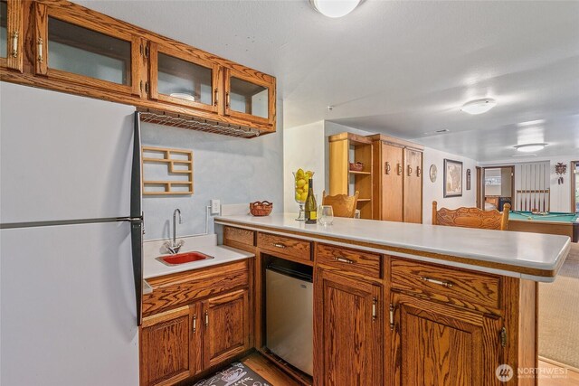 kitchen with brown cabinets, a sink, fridge, freestanding refrigerator, and a peninsula