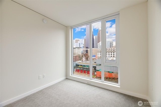 unfurnished room featuring a city view, baseboards, and carpet