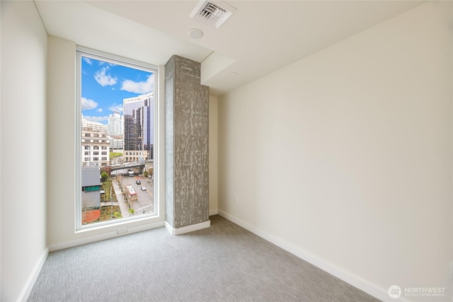 carpeted empty room featuring a view of city, a healthy amount of sunlight, visible vents, and baseboards