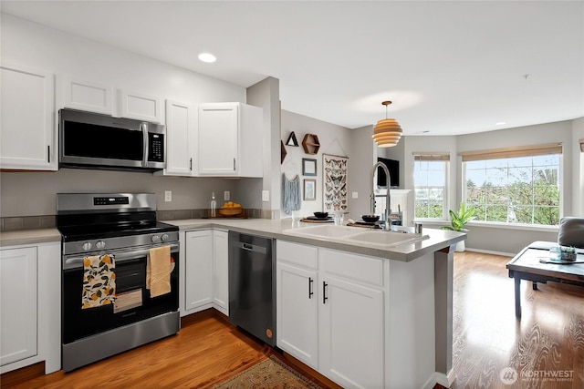 kitchen featuring white cabinets, appliances with stainless steel finishes, a peninsula, and a sink