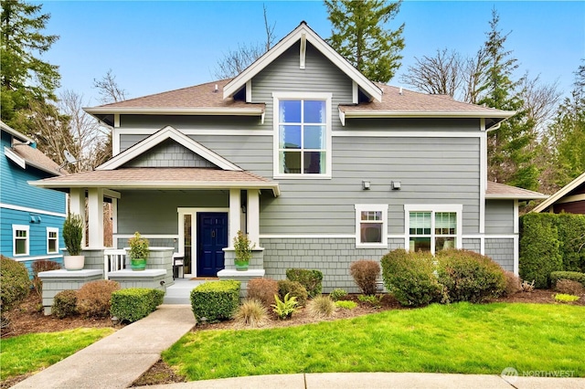 view of front of property with a porch, a front lawn, and roof with shingles