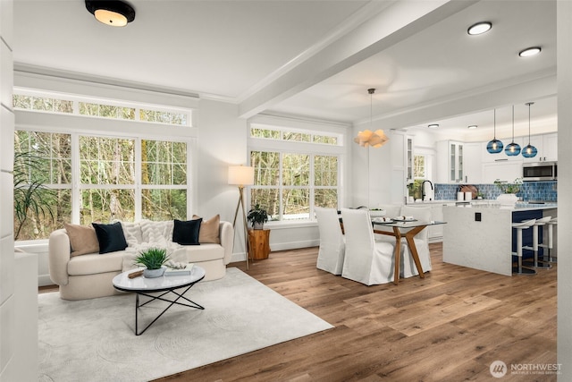 living area featuring beam ceiling, wood finished floors, baseboards, and ornamental molding