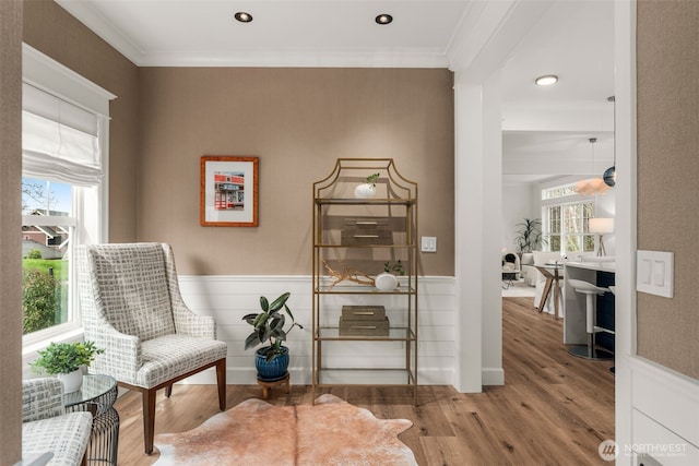 living area with plenty of natural light, wood finished floors, wainscoting, and crown molding