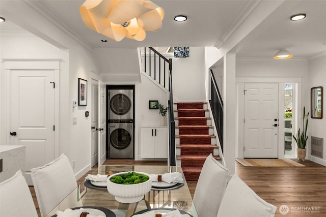 foyer featuring visible vents, stairs, ornamental molding, stacked washing maching and dryer, and wood finished floors