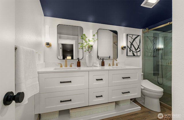 bathroom featuring wood finished floors, double vanity, a sink, a shower stall, and toilet