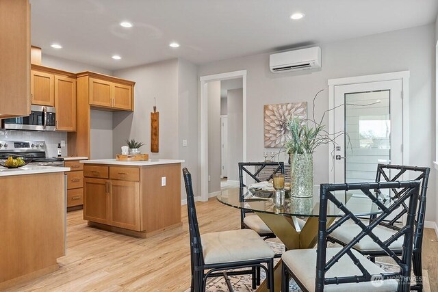 kitchen featuring appliances with stainless steel finishes, light wood-style flooring, light countertops, and a wall unit AC