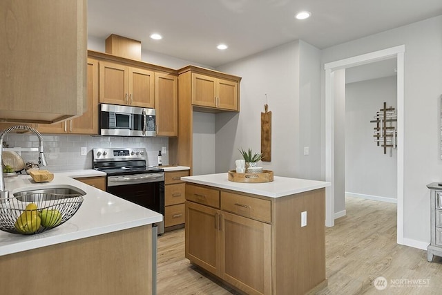 kitchen featuring light wood-style flooring, a sink, backsplash, appliances with stainless steel finishes, and light countertops