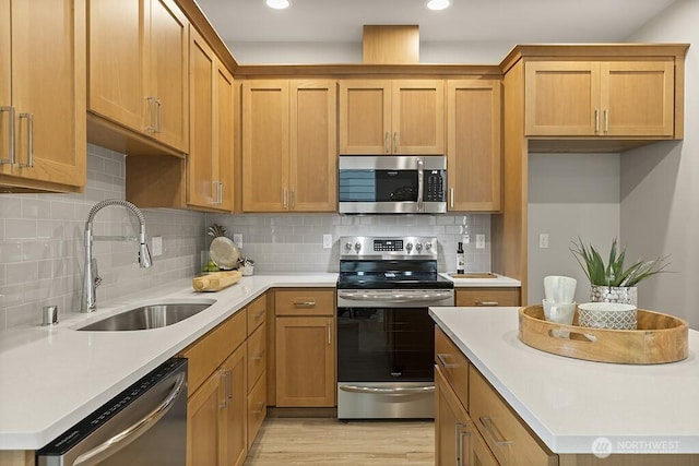 kitchen with a sink, backsplash, stainless steel appliances, light wood-style floors, and light countertops