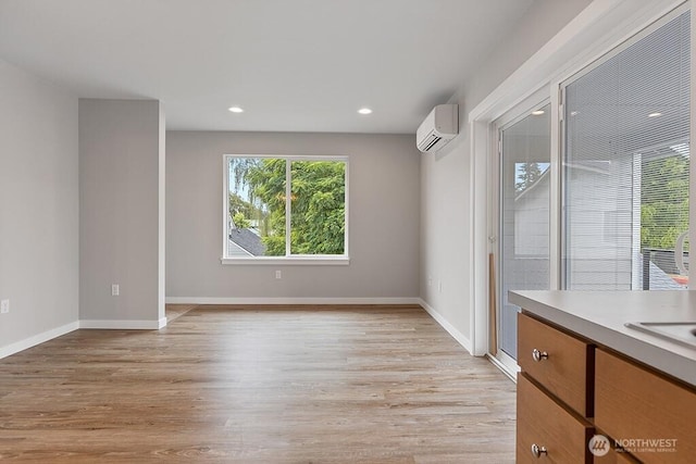 empty room with recessed lighting, light wood-type flooring, baseboards, and a wall unit AC