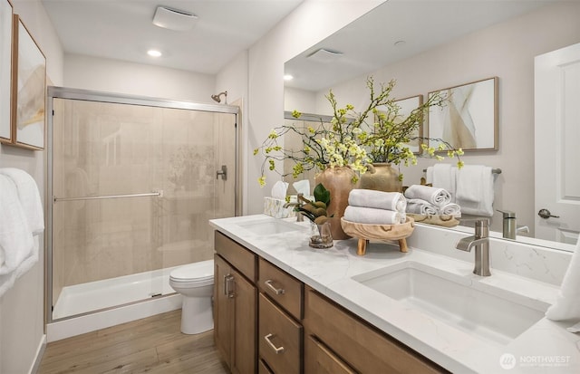 bathroom with toilet, a stall shower, wood finished floors, and a sink