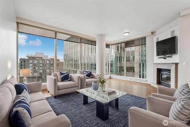 living area featuring a glass covered fireplace, a view of city, floor to ceiling windows, and wood finished floors