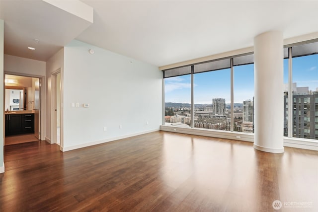 unfurnished room featuring baseboards, a city view, dark wood finished floors, and floor to ceiling windows