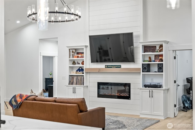 living area with light wood-type flooring, a glass covered fireplace, and a towering ceiling