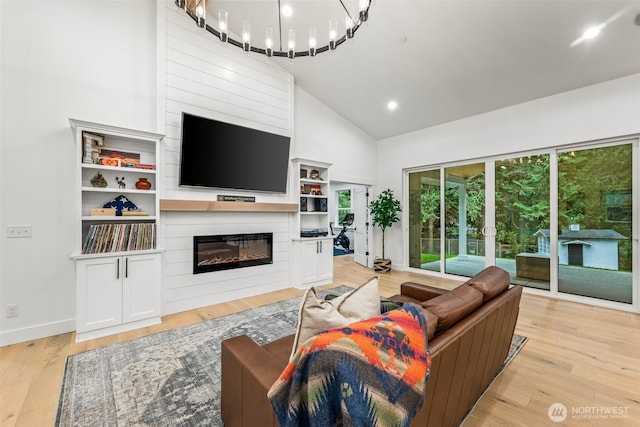 living area with high vaulted ceiling, a glass covered fireplace, light wood-style floors, an inviting chandelier, and baseboards