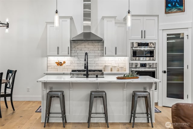 kitchen with tasteful backsplash, a breakfast bar, wall chimney exhaust hood, and a kitchen island with sink