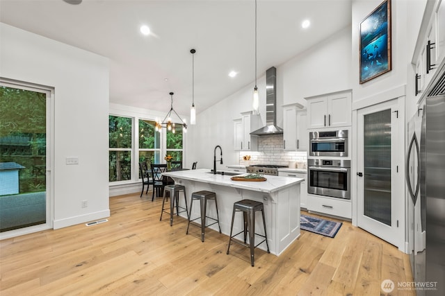 kitchen featuring visible vents, light stone countertops, a breakfast bar area, wall chimney exhaust hood, and a sink