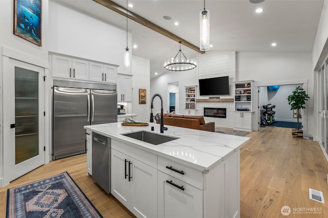 kitchen with a sink, stainless steel appliances, light wood-type flooring, and a fireplace