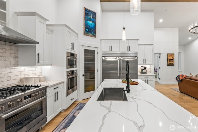 kitchen featuring decorative light fixtures, light wood-type flooring, high end appliances, a high ceiling, and wall chimney exhaust hood