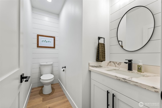 half bathroom featuring vanity, toilet, wood finished floors, and baseboards