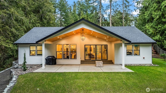 back of house featuring a patio area, a lawn, and a shingled roof