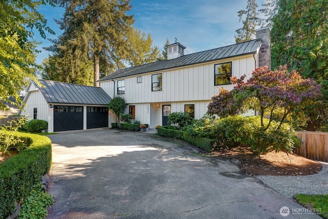 view of front of property featuring driveway, a standing seam roof, an attached garage, a chimney, and metal roof