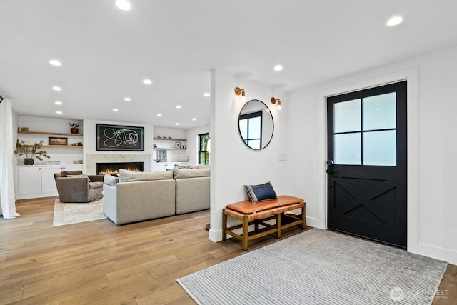 foyer entrance featuring a lit fireplace, recessed lighting, baseboards, and light wood-style floors