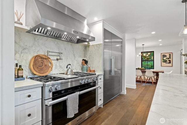 kitchen with hardwood / wood-style flooring, backsplash, white cabinets, wall chimney range hood, and high end appliances