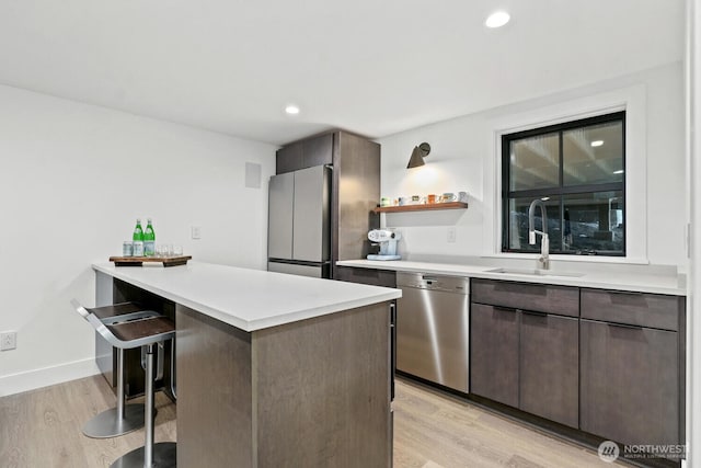 kitchen featuring light wood finished floors, a kitchen breakfast bar, stainless steel dishwasher, freestanding refrigerator, and a sink