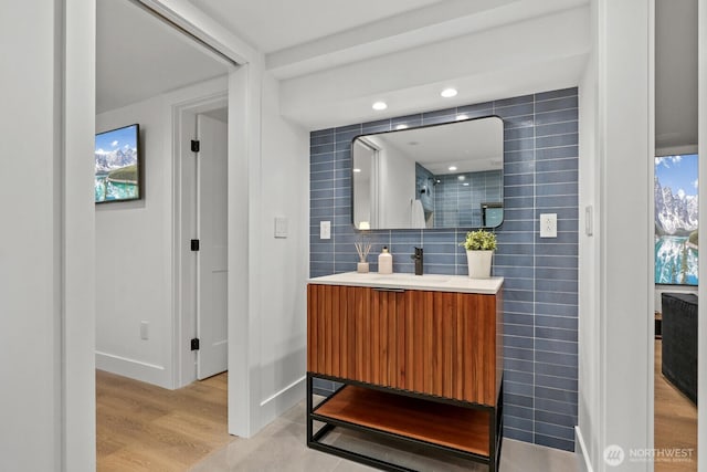 full bathroom with baseboards, a tile shower, decorative backsplash, wood finished floors, and vanity