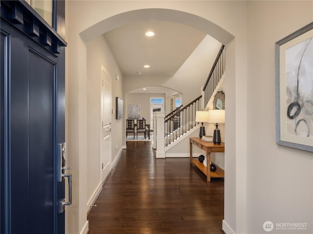 entrance foyer featuring dark wood-style floors, baseboards, recessed lighting, arched walkways, and stairs