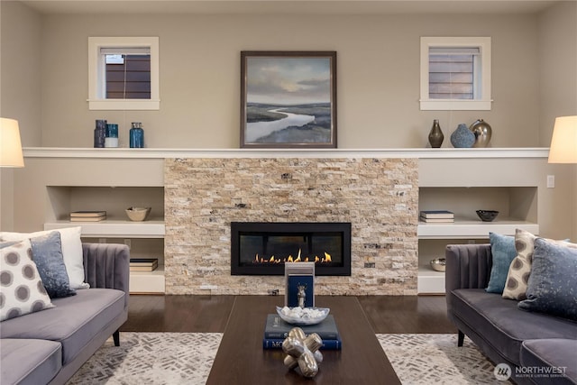 living room with a stone fireplace, built in shelves, and wood finished floors