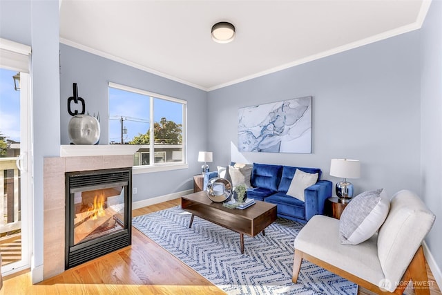 living room with a tile fireplace, crown molding, baseboards, and wood finished floors