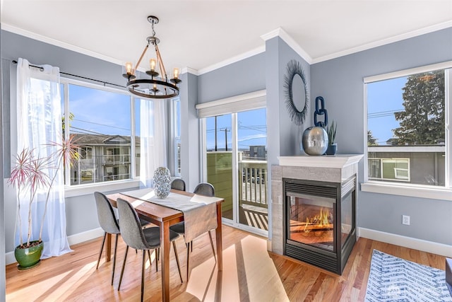 dining area with crown molding, baseboards, a multi sided fireplace, wood finished floors, and a notable chandelier