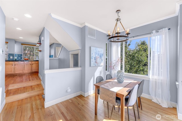 dining room with visible vents, baseboards, light wood finished floors, and ornamental molding