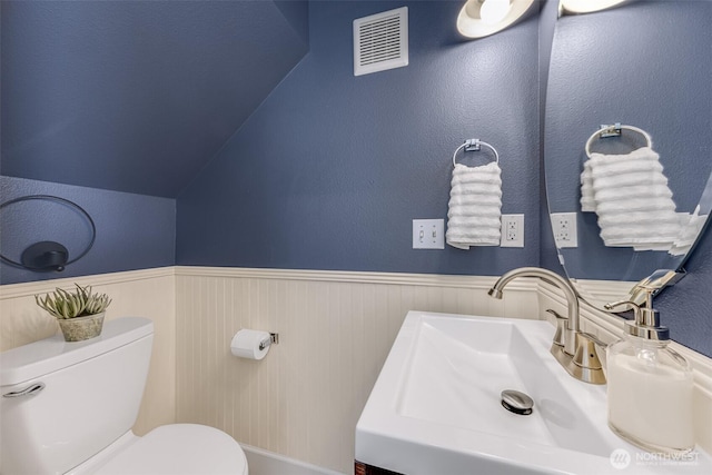 bathroom with a sink, visible vents, toilet, and a wainscoted wall