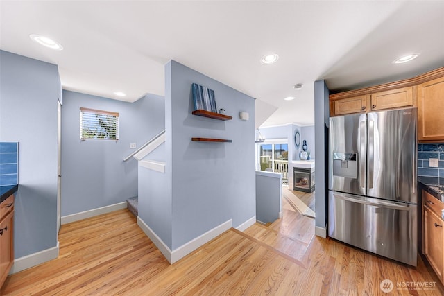 kitchen with baseboards, light wood finished floors, stainless steel fridge with ice dispenser, a glass covered fireplace, and dark countertops