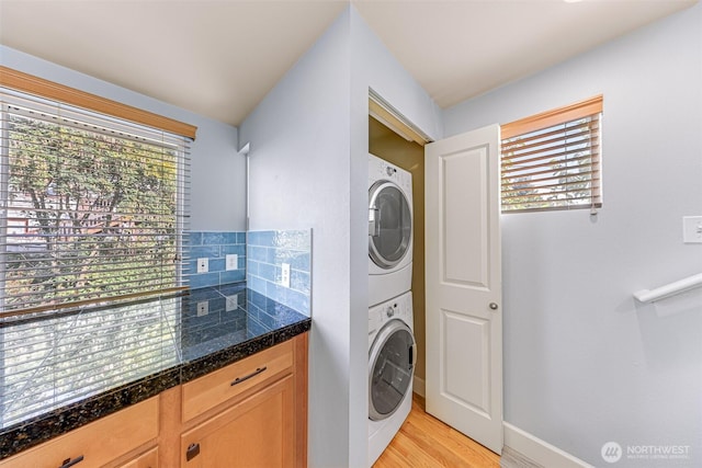 laundry area with stacked washer / drying machine, baseboards, laundry area, and light wood finished floors