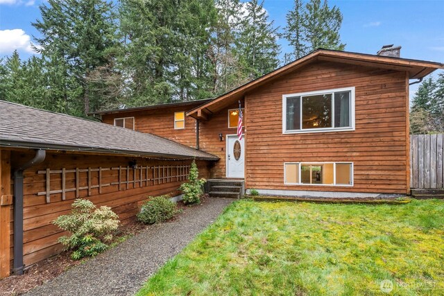 view of front of property with fence, a shingled roof, entry steps, a front lawn, and a chimney