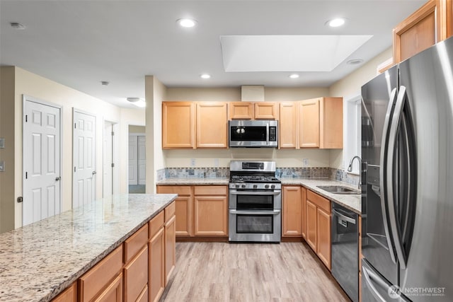 kitchen with light brown cabinets, a skylight, a sink, stainless steel appliances, and light wood-style floors