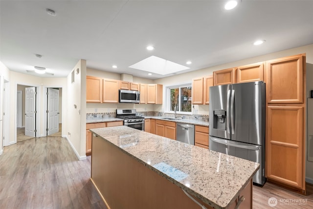 kitchen with light wood-style flooring, light brown cabinets, a sink, stainless steel appliances, and a skylight