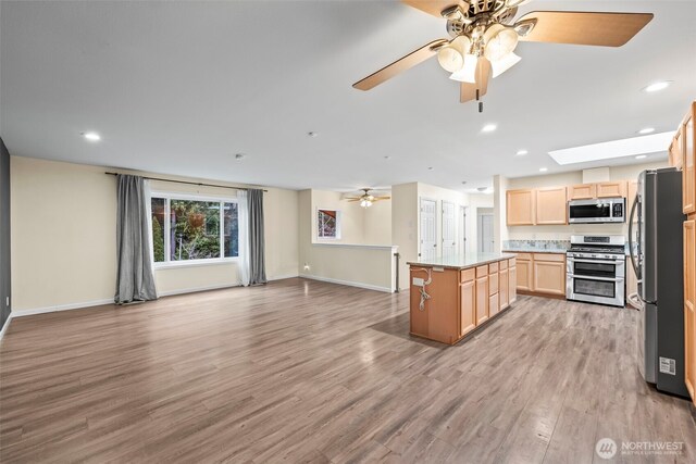 kitchen featuring light brown cabinets, light wood finished floors, stainless steel appliances, open floor plan, and a center island